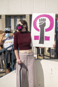 Megan Hughes holds a sign with a raised fist inside a female sign.