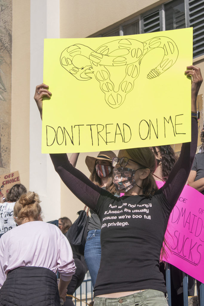 Romi Hitchcock-Tinseth holds a sign with a snake in the shape of a uterus saying "don't tread on me".