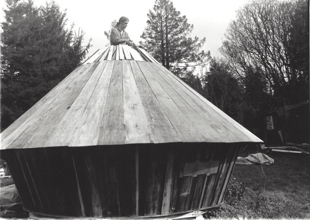 A black and white photo of the finishing touches being put on the roof of the yurt.