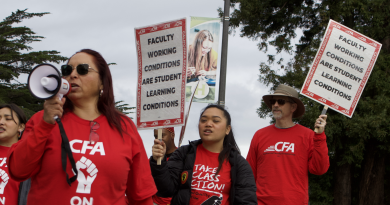 Faculty and students cross the street in red shirts holding signs. The professor in the front holds a megaphone. Student and CFA member behind her hold signs that read "faculty working conditions are student learning conditions."