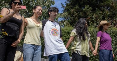 Image of five people embracing in a line. Outside, at immigrant rights event.