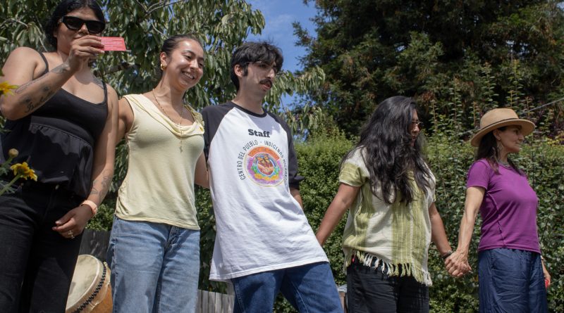 Image of five people embracing in a line. Outside, at immigrant rights event.