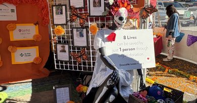 An altar is shown at a Dia de muertos festival. There is a skeleton in front of the altar holding a sign that says, "8 lives can be saved by just every 1 person through organ donation."